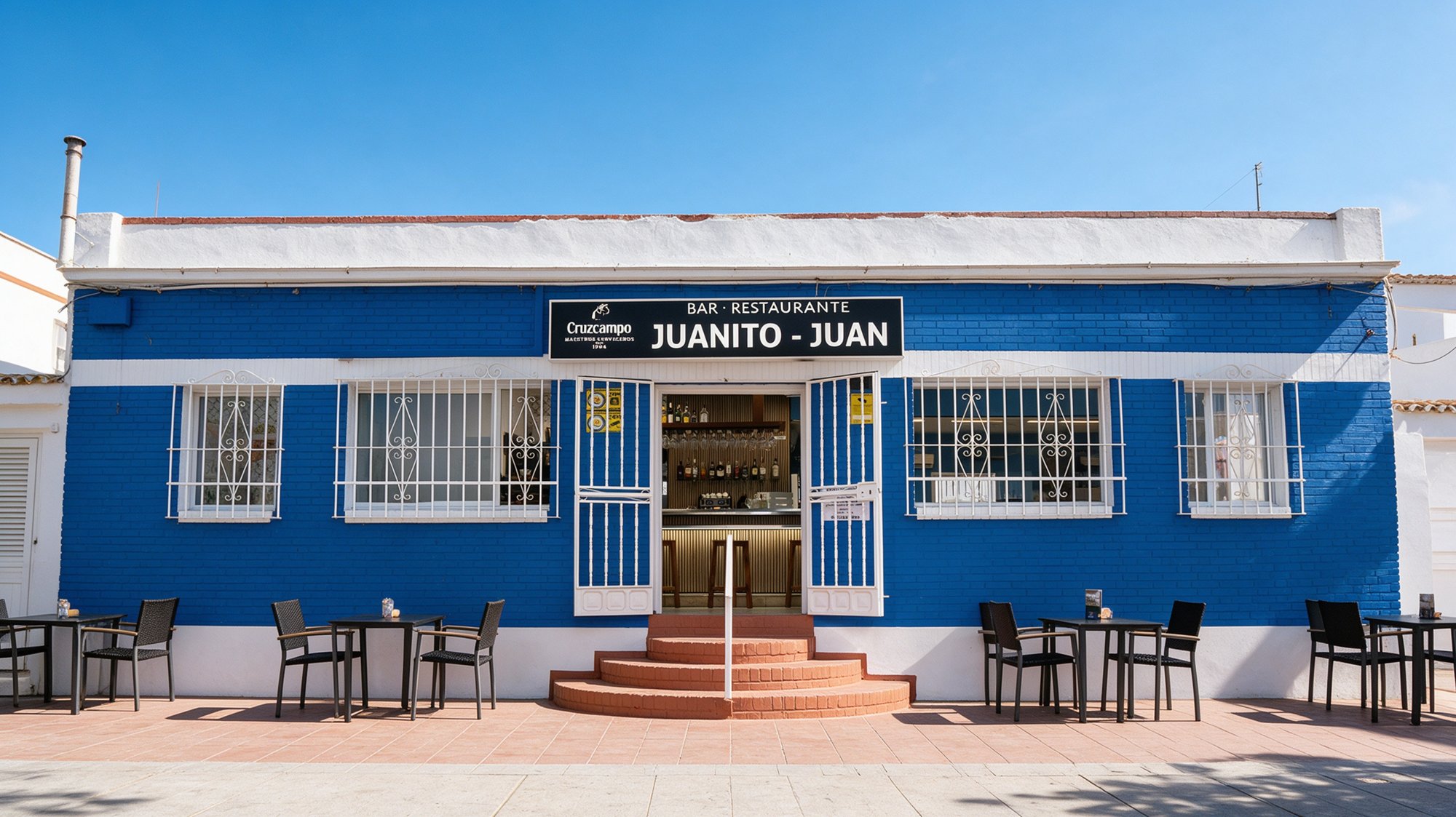 Fachada azul y blanca de restaurante de pescado con rótulo negro que dice Restaurante Juanito-Juan y barra al fondo